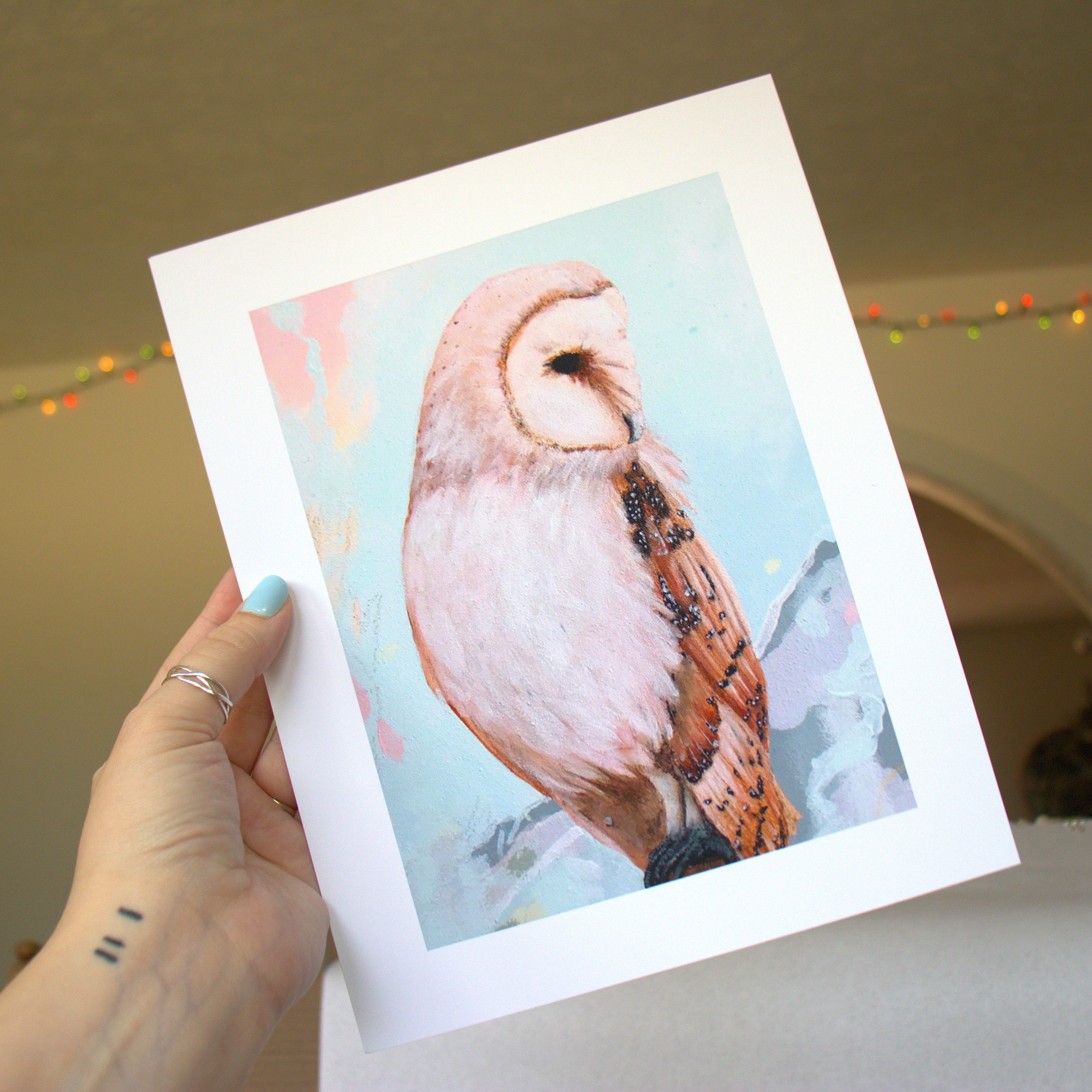 Hand holding a print with an owl illustration against a neutral background