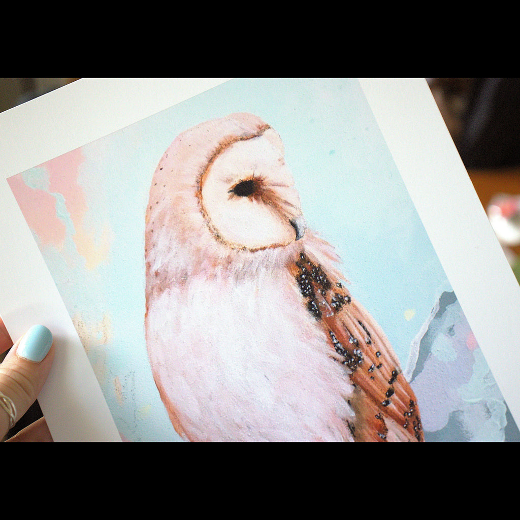 Hand holding a print of an owl with a soft pastel background