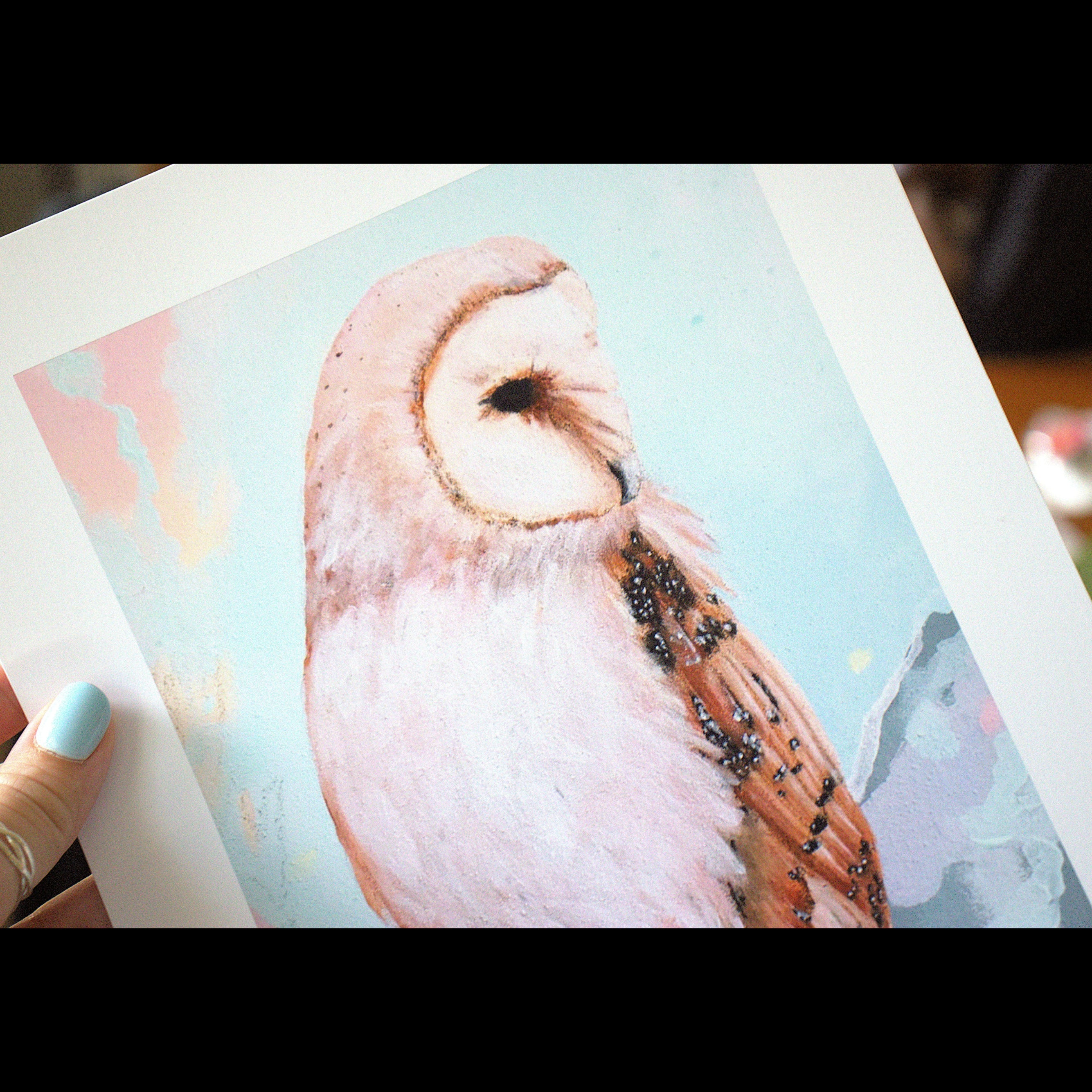 Hand holding a print of an owl with a soft pastel background